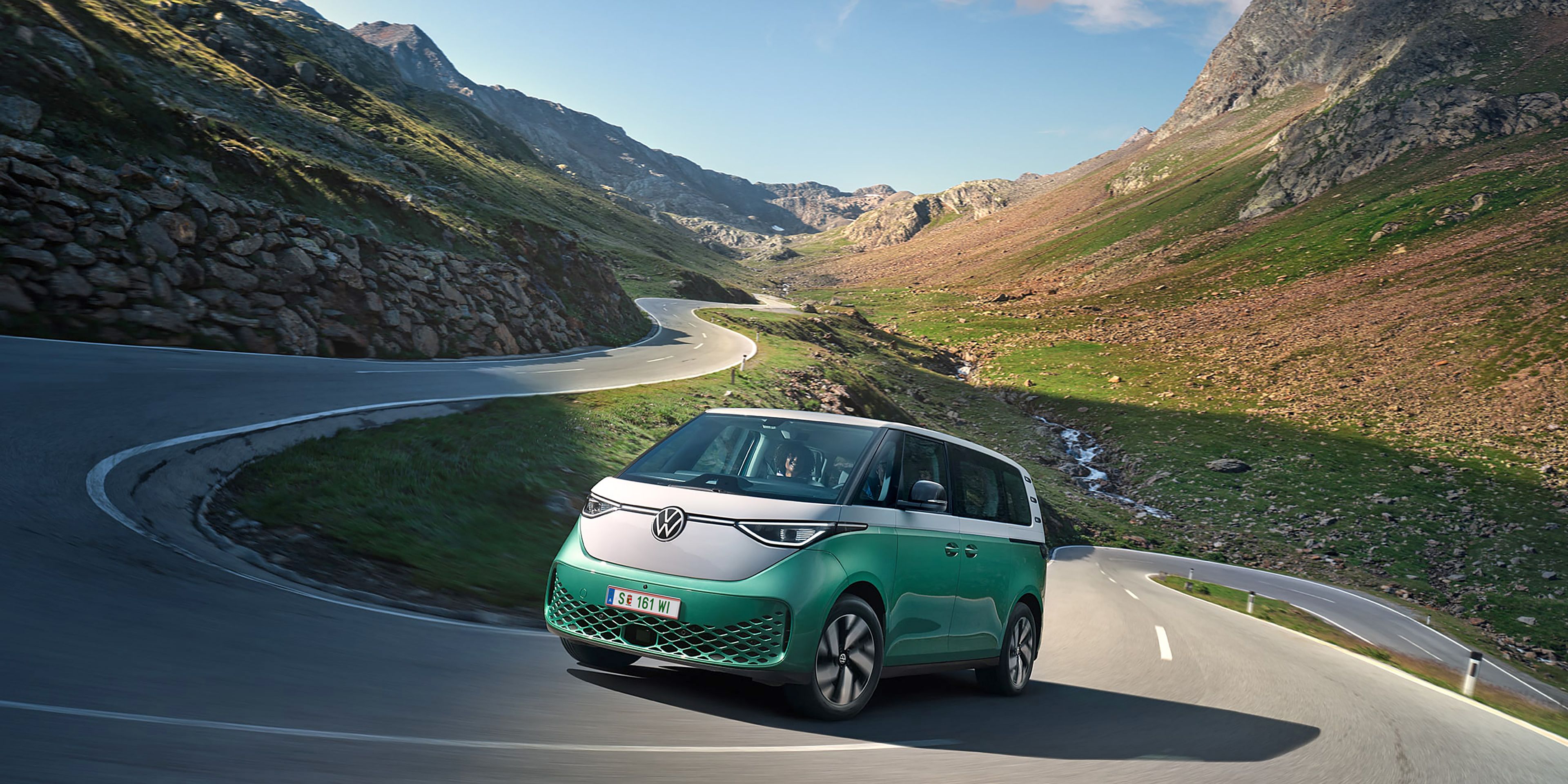 Ein grün weißer VW ID. Buzz fährt dynamisch in die Kurve einer kurvenreichen Bergstraße