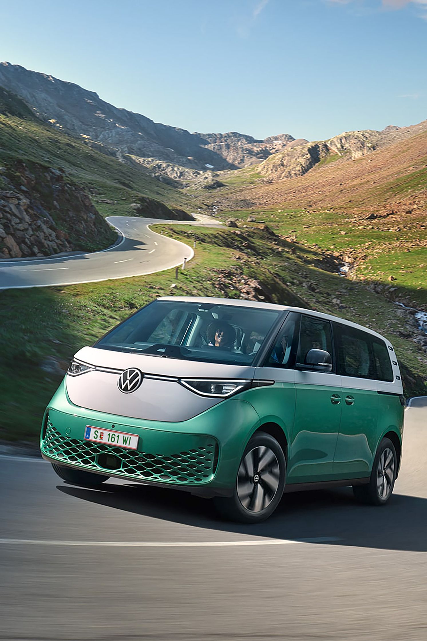 Ein grün weißer VW ID. Buzz fährt dynamisch in die Kurve einer kurvenreichen Bergstraße