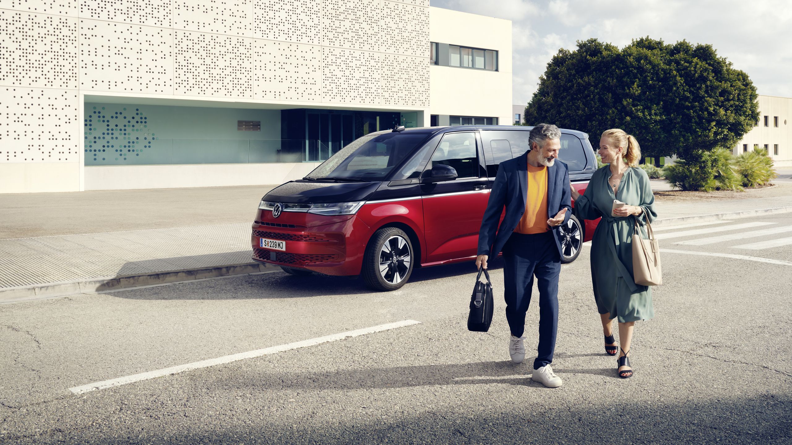 Ein Paar läuft vor einem neuen VW Multivan T7 2021 Style. 