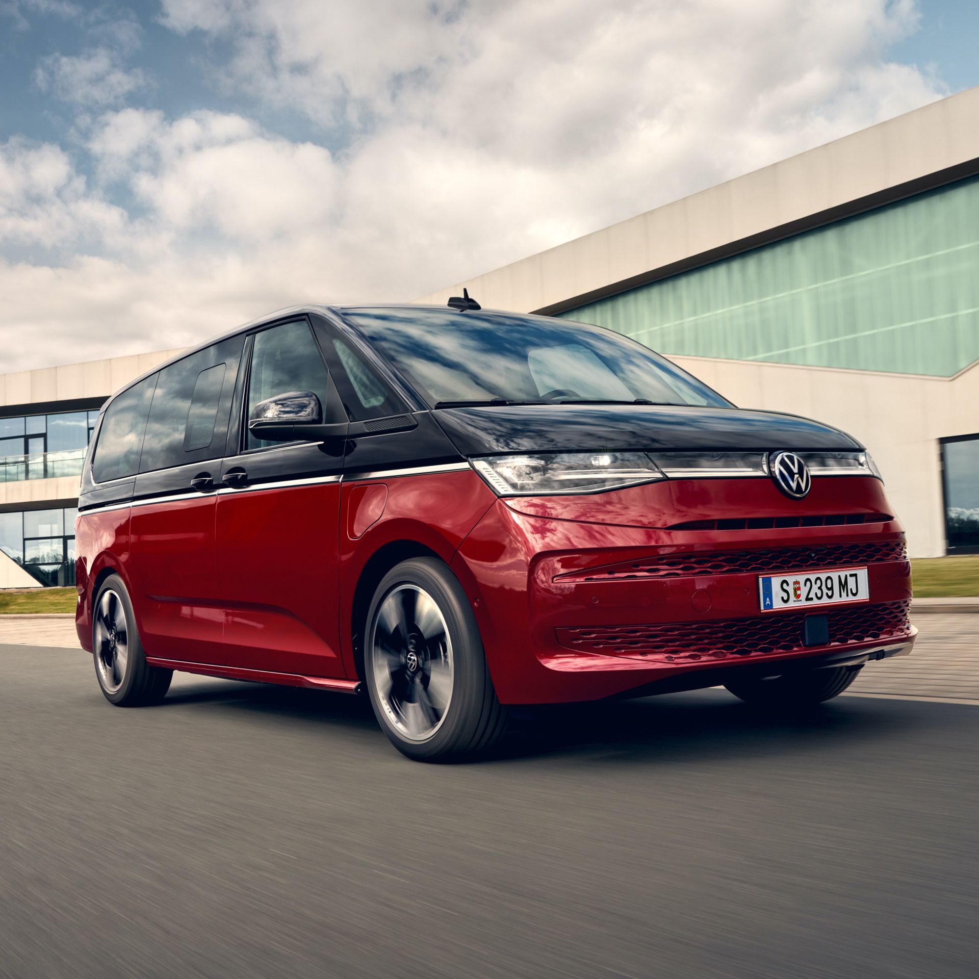 Der VW Multivan Style T7 2021 vor einem Gebäude aus Glas. 
