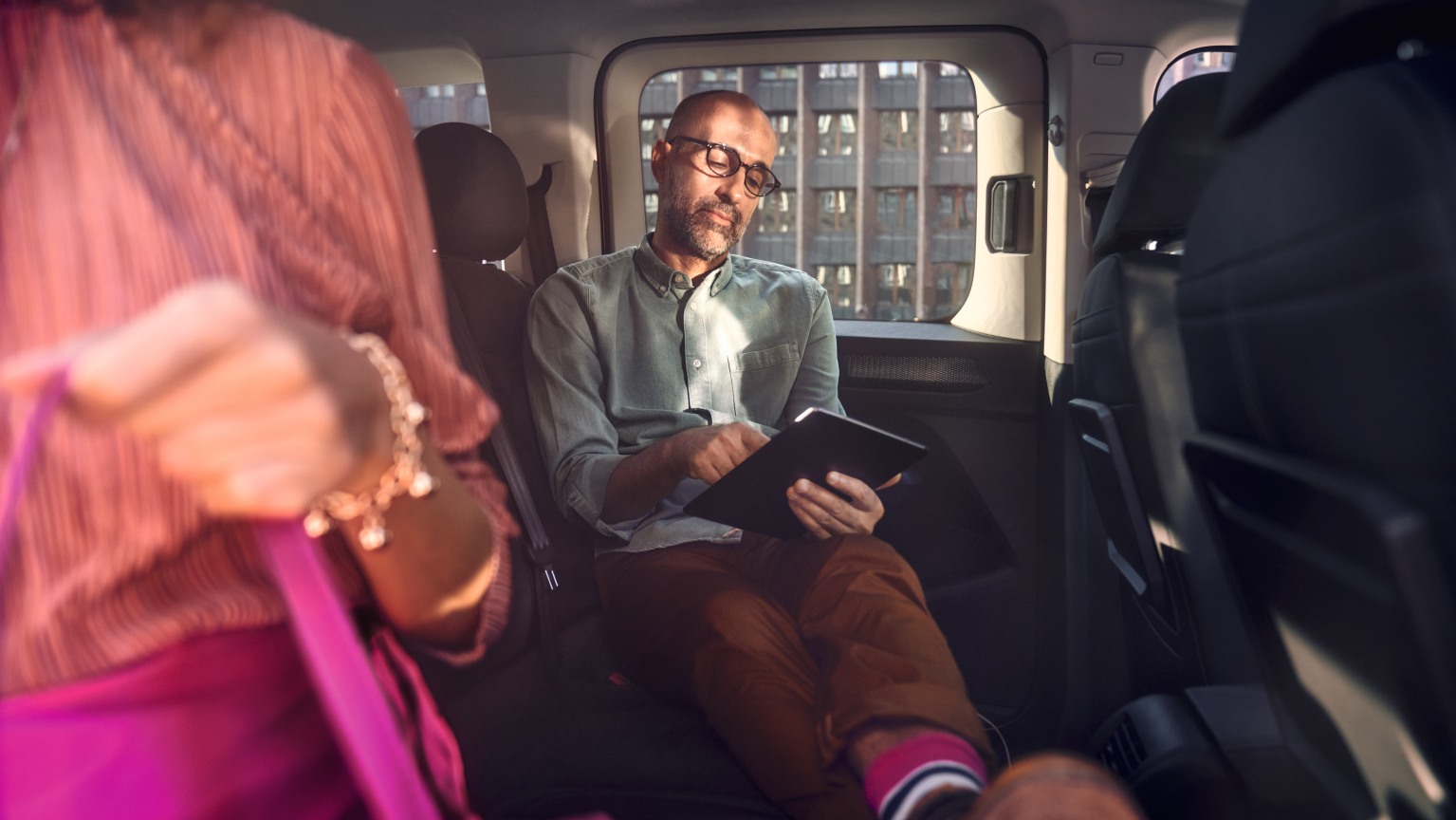 Mann sitzt in VW Caddy und liest auf Tablet.