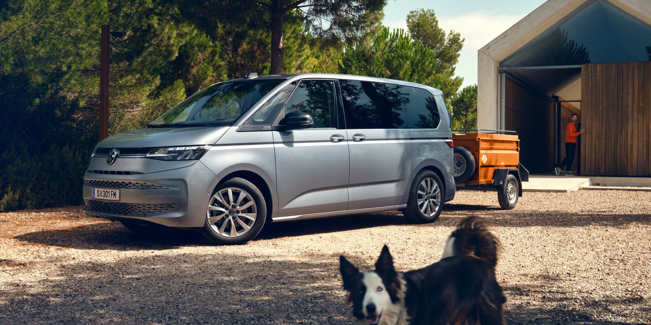 Der neue VW T7 Multivan in Silber steht vor Scheune und Hund lauft vorbei