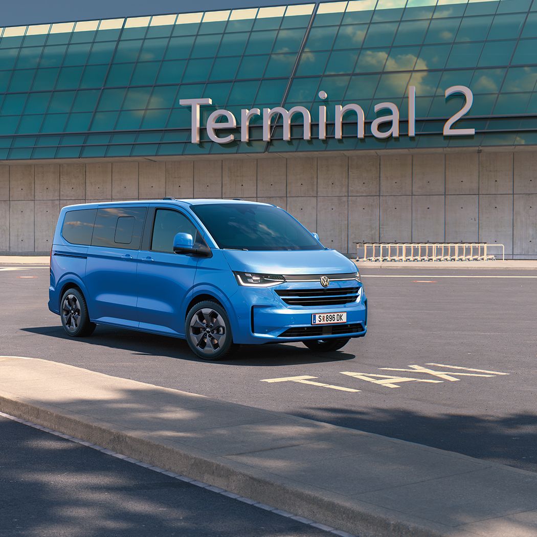 Zwei VW Caravelle stehen vor dem Terminal 2 auf einem Flughafenparkplatz