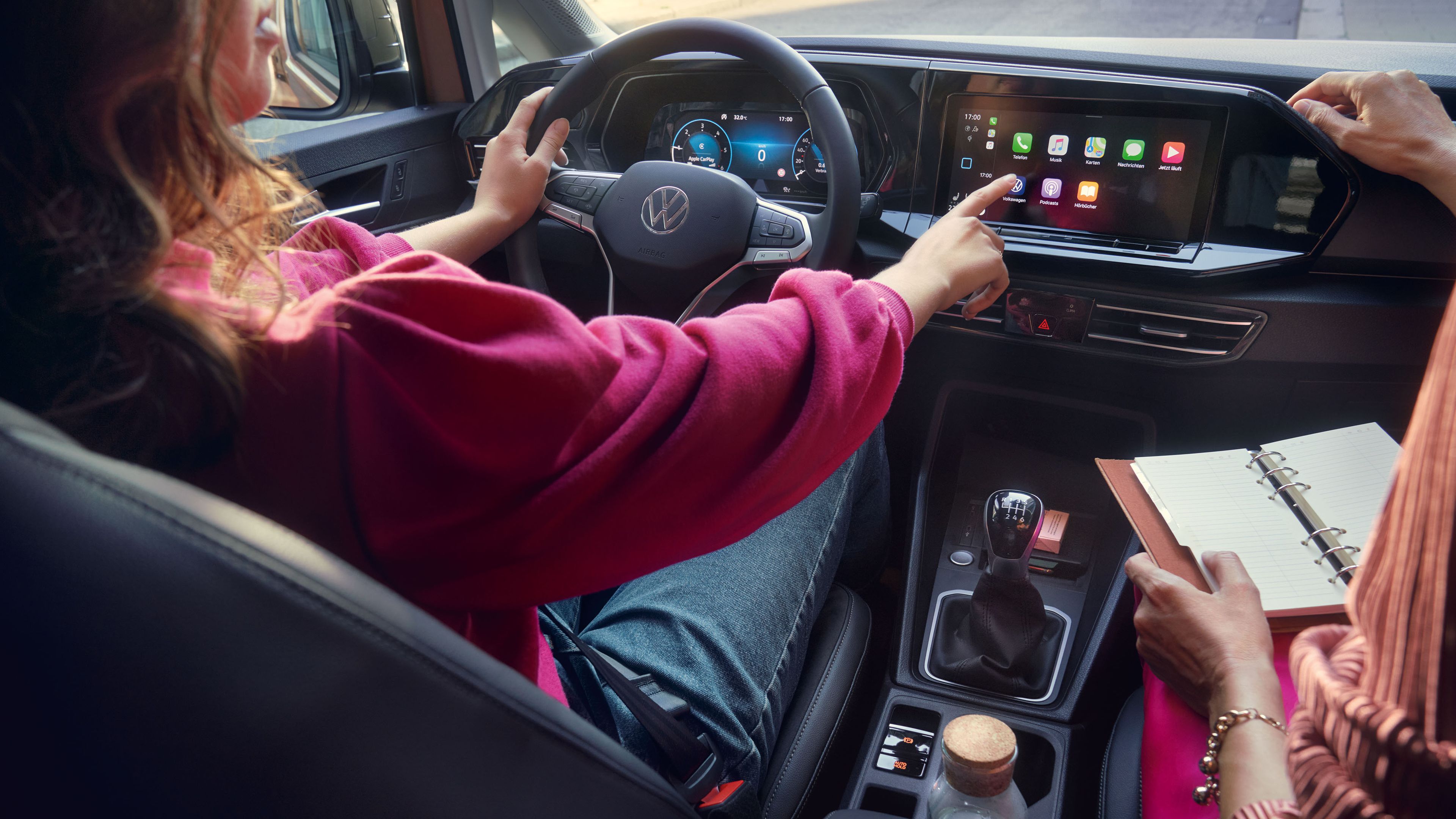 Frau sitzt im VW Caddy California und bedient das Display. 
