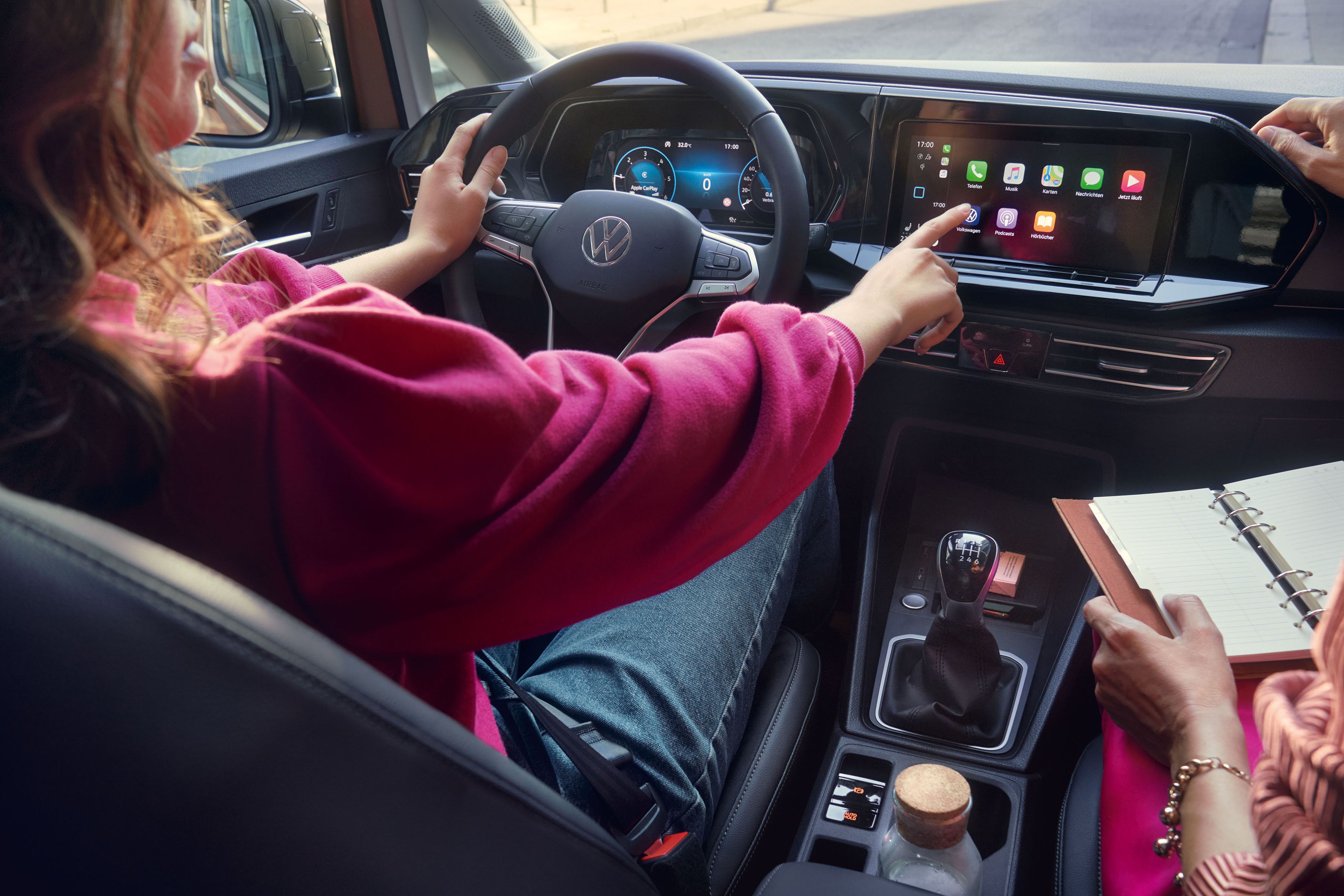 Frau sitzt im VW Caddy California und bedient das Display. 